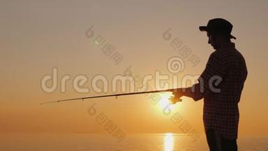 日落时在海滩上钓鱼的年轻渔夫的剪影。 侧视图